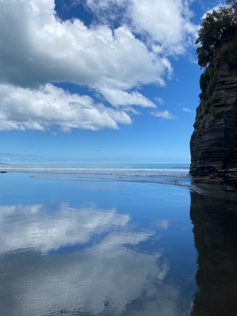 Reflected sky on black sand with waves at Three Sisters Beach Taranaki